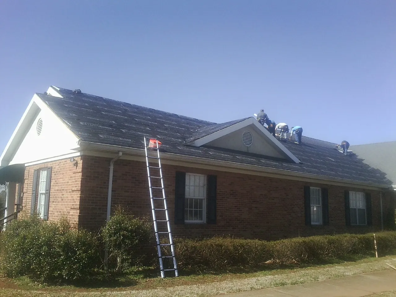Crew tearing shingles off a brick ranch roof with a ladder set — Metal Roof Repair work by our crew in Daphne