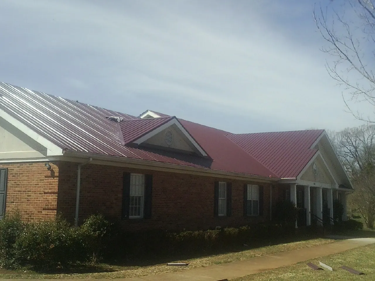 Red metal roof with gabled entries on a long brick building, from a Hail Damage Roof Repair job in Daphne