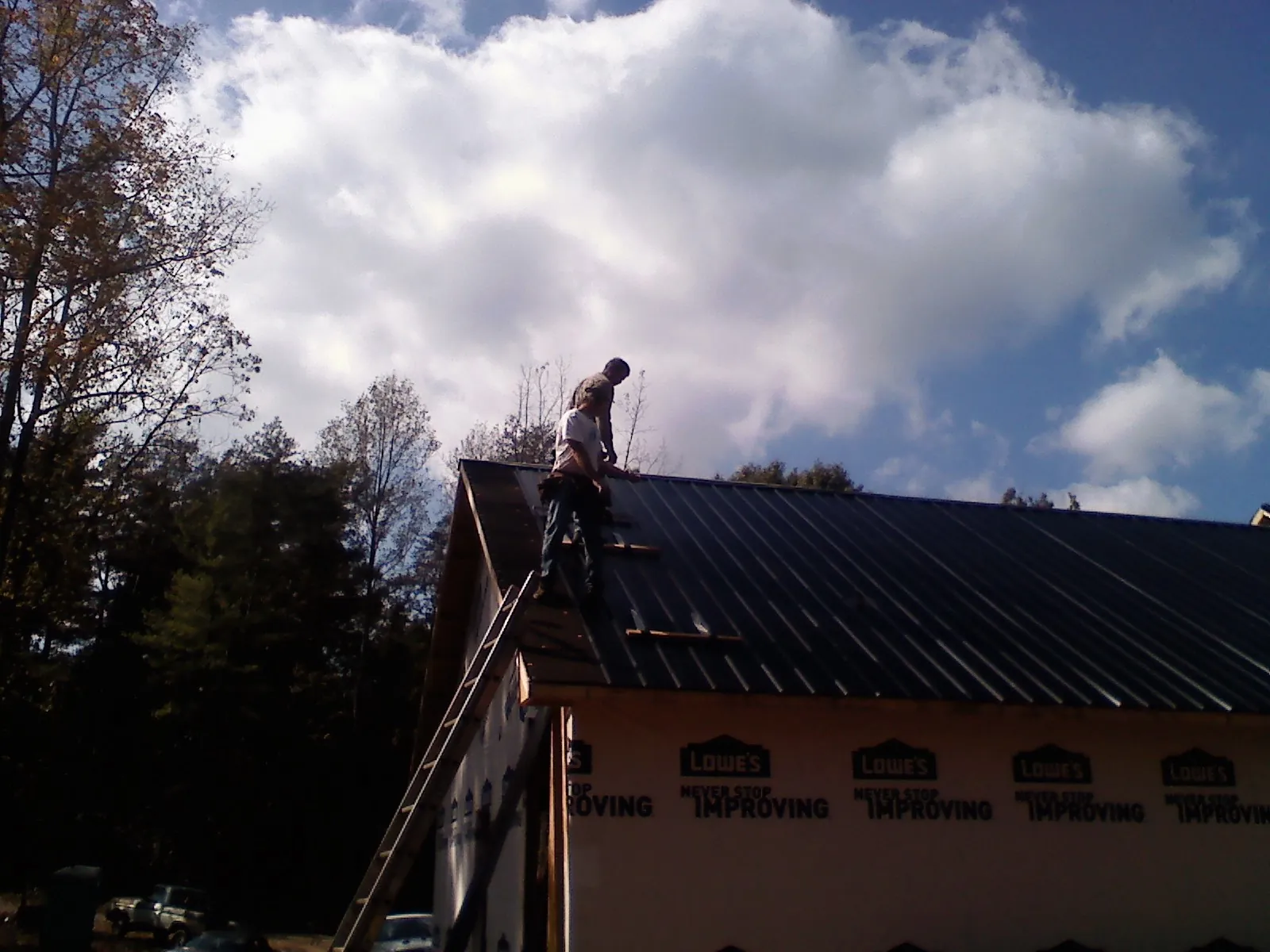 Roofer fastening dark metal panels high against a cloudy sky, from a Roof Inspection job in Daphne