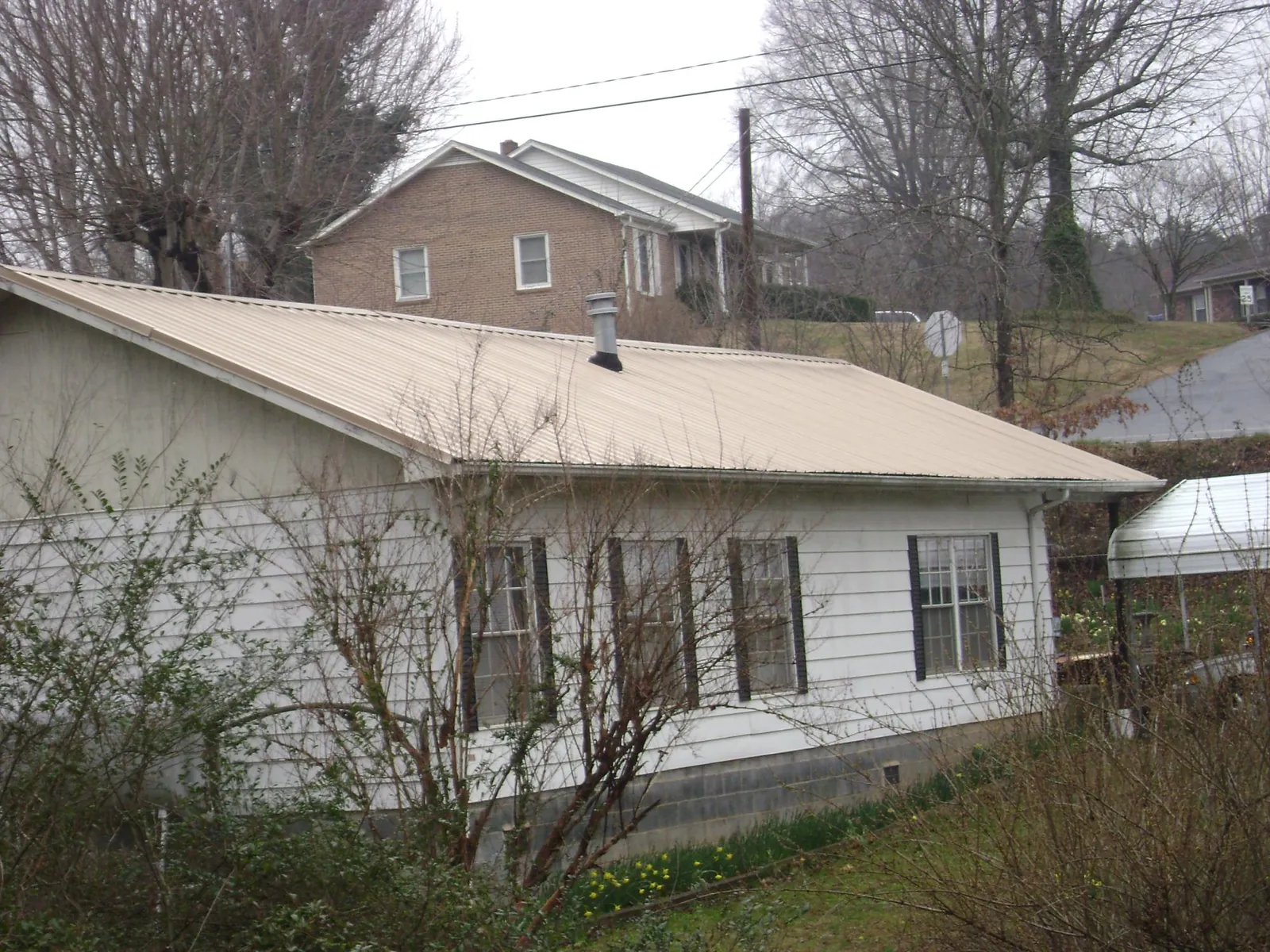 Tan metal roof on a white sided house set into a hillside — Commercial Roofing by Roofing Brothers in Daphne