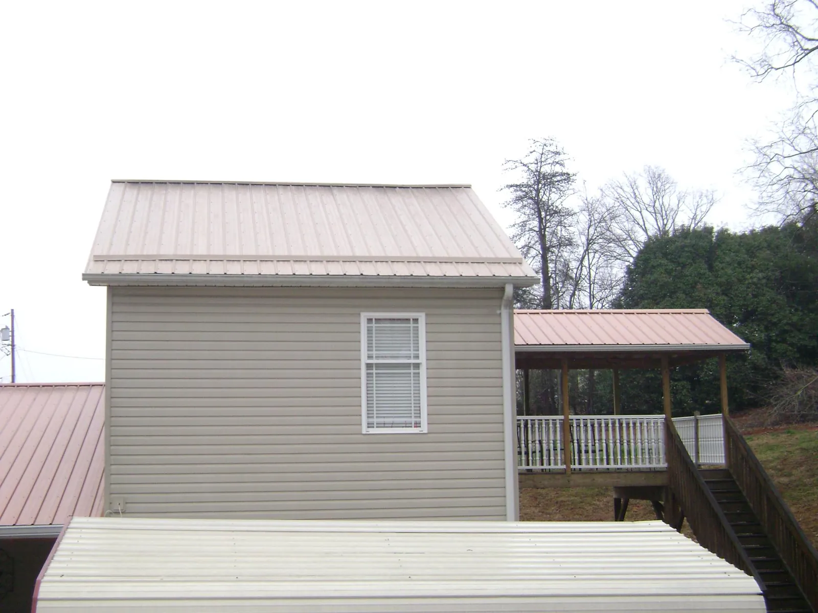 Tan metal roofs on a two story addition and attached porch, from a Roof Replacement job in Daphne